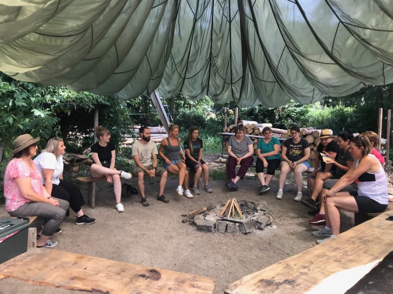 Teamentwicklung & Teambuiling Gruppe sitzt um Feuerstelle in der Natur während einem Teamtag